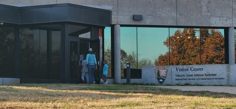 People outside of a building with concrete, columns and large windows.