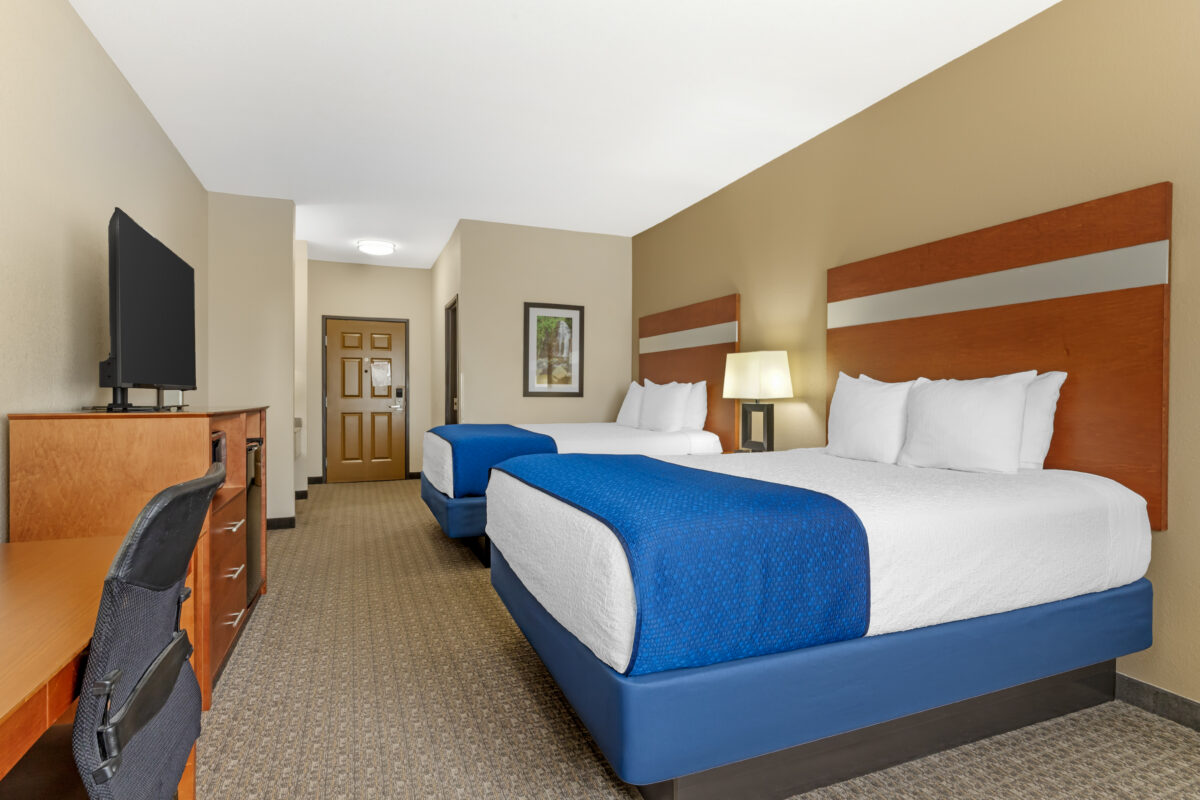 A furnished hotel bedroom with two beds, a desk and a television and blue tones.