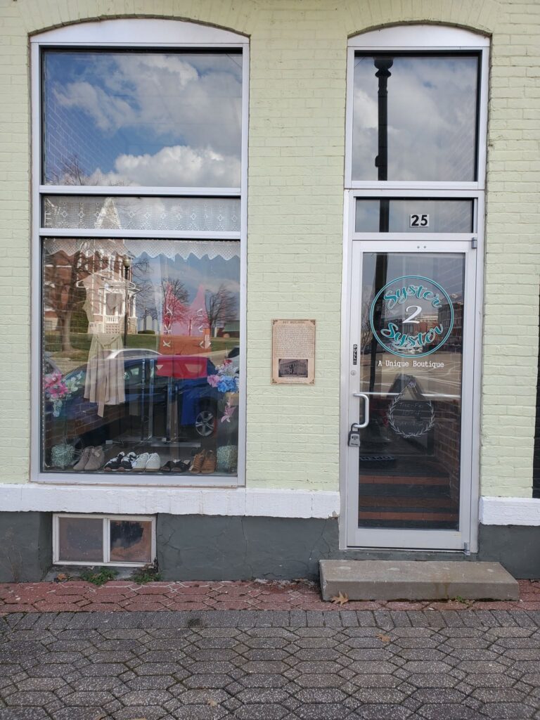 The outside of a boutique with a tall display window and glass door.