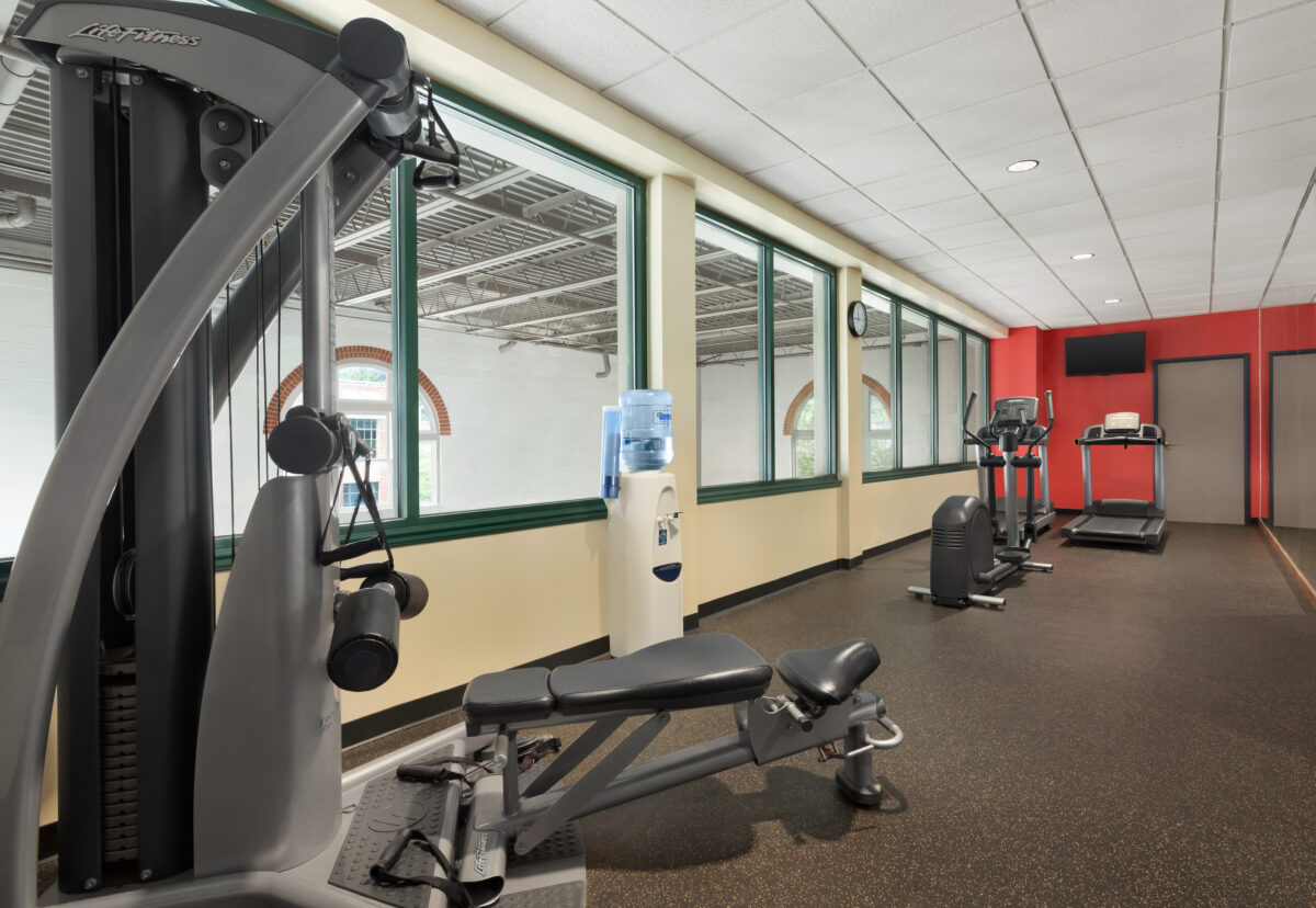 A hotel gym with equipment and a far red wall.