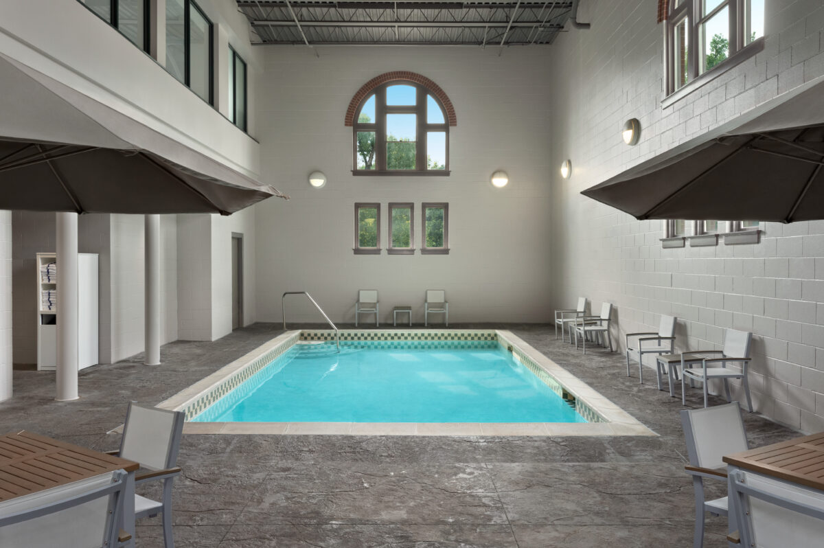 An indoor pool with tall ceiling, grey interior and very blue water.