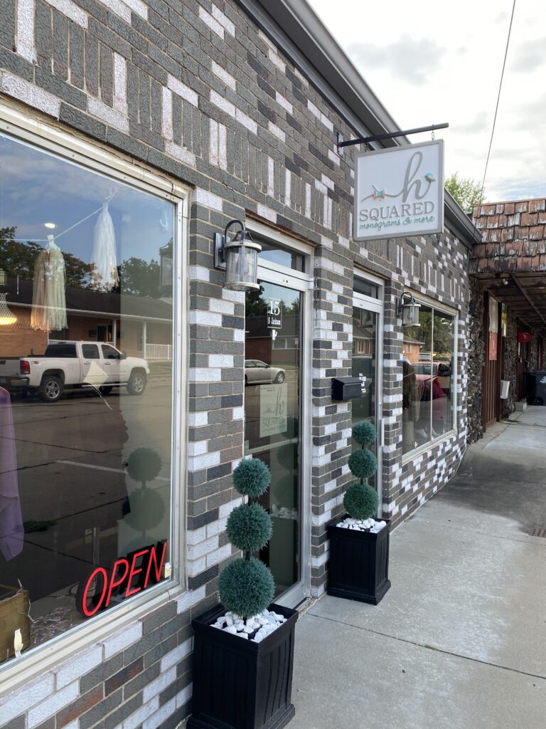 A store front with brick and stone work, large windows and plants out front.