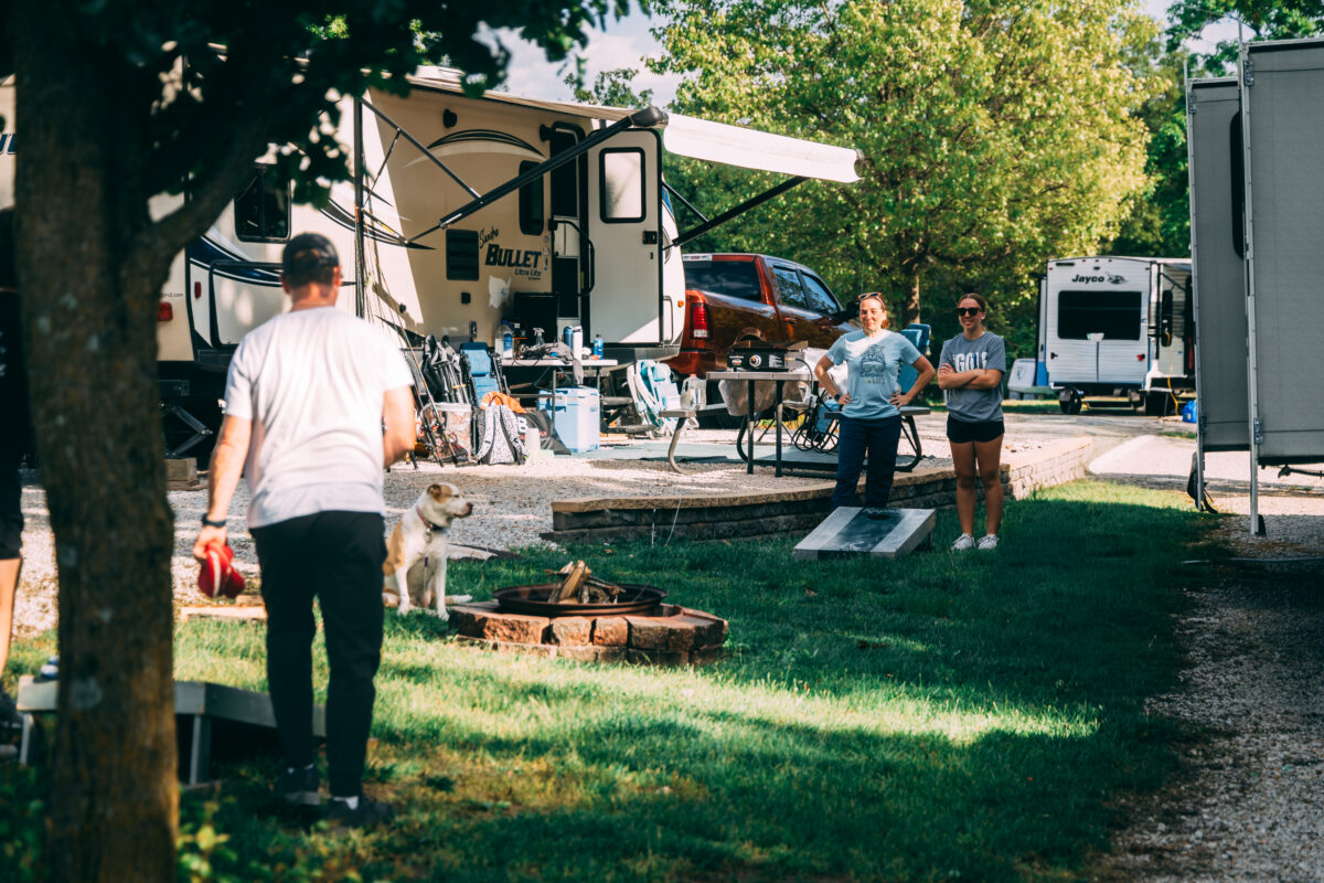 Campers set in the woods with people playing cornhole.