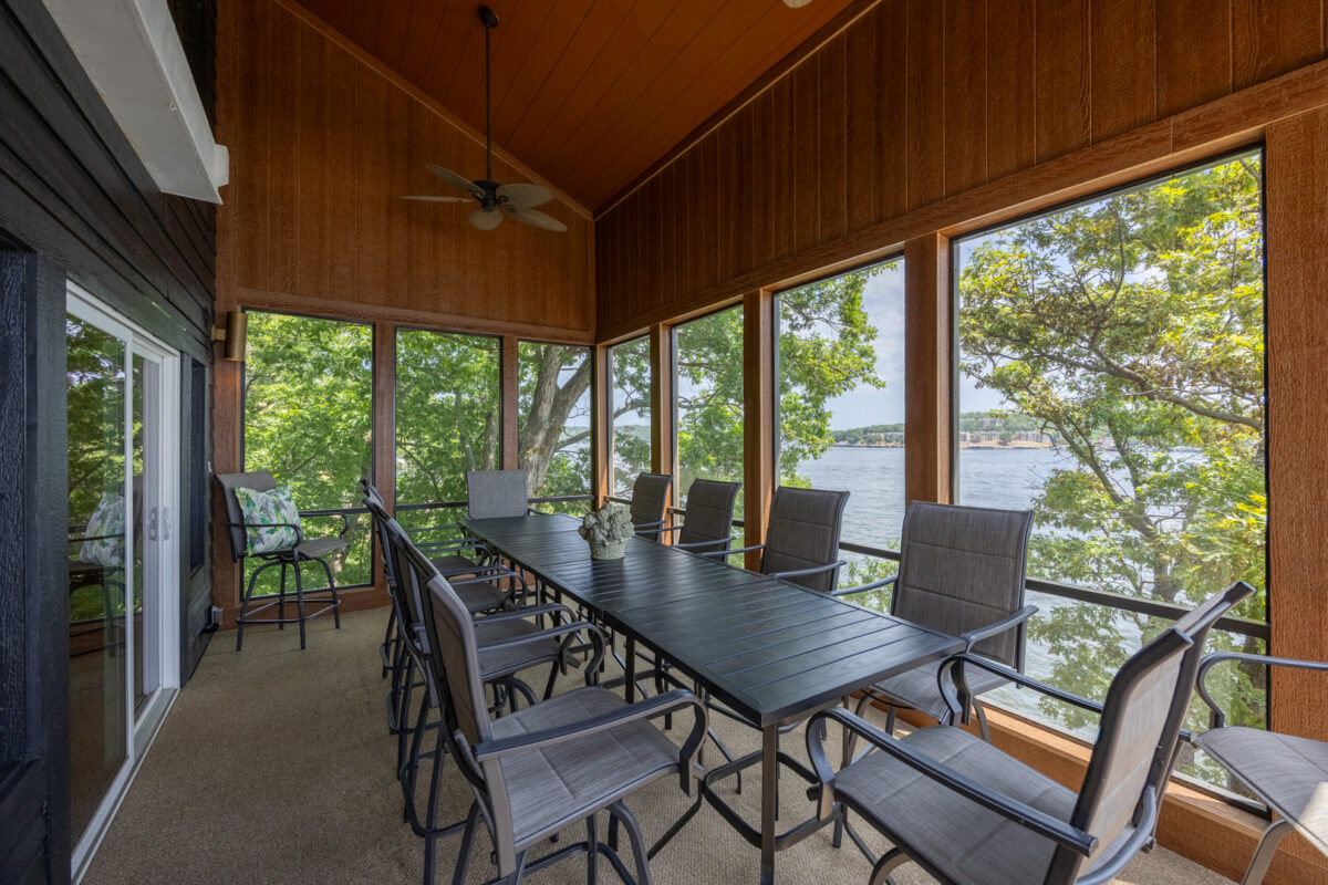 A table and chairs in a sunroom with a view of trees.