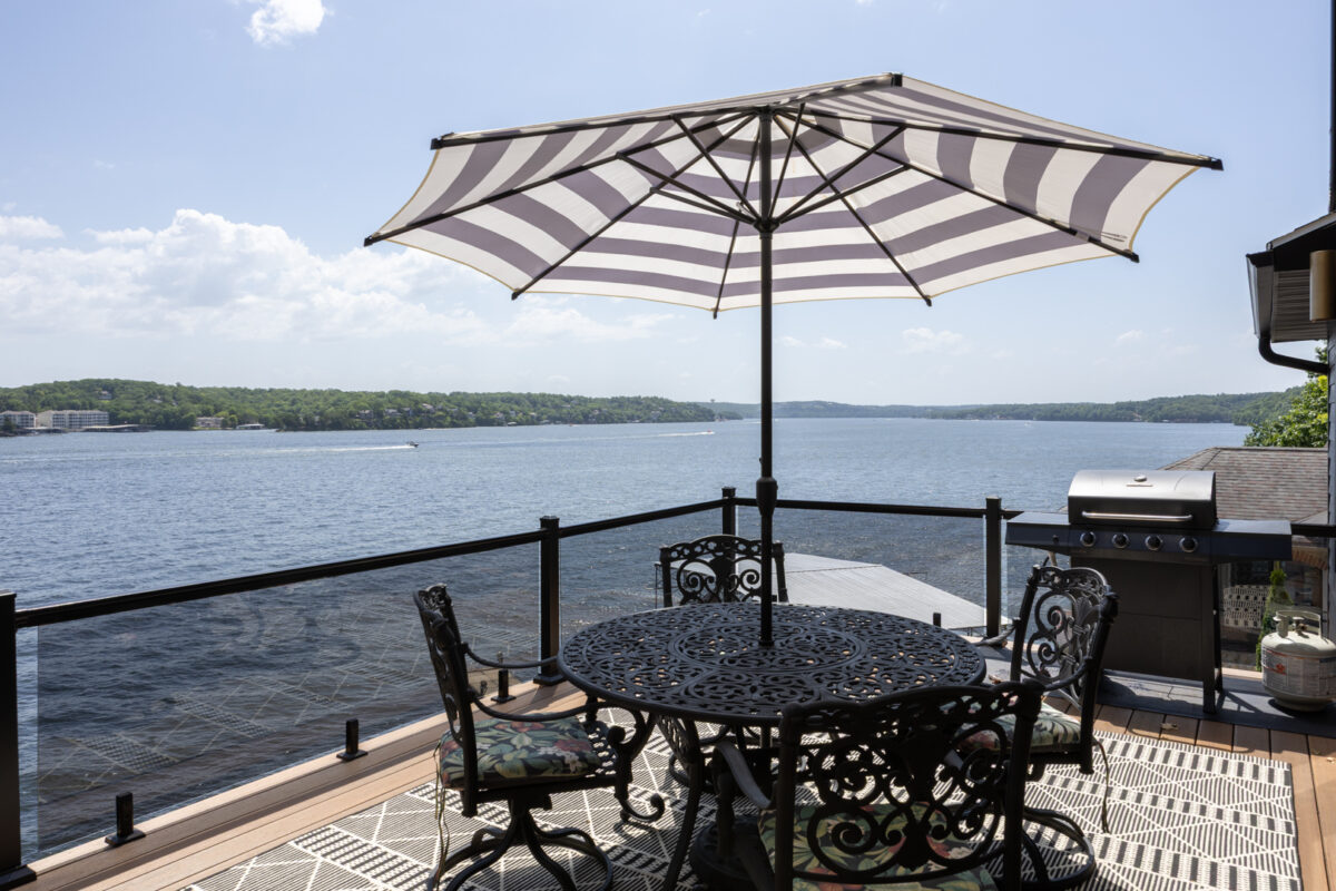 A patio with furniture and a large umbrella near a lake.