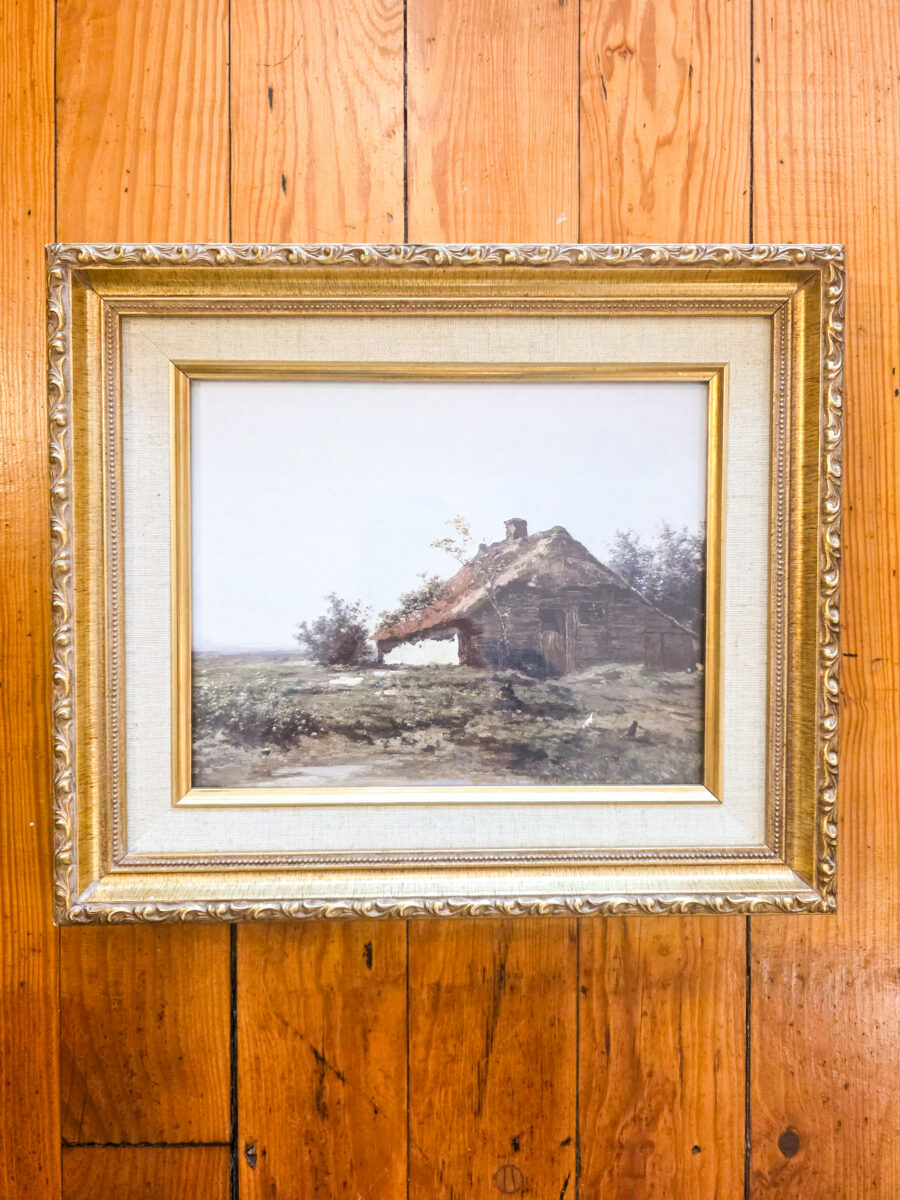 A painting framed against a wood-paneled wall.