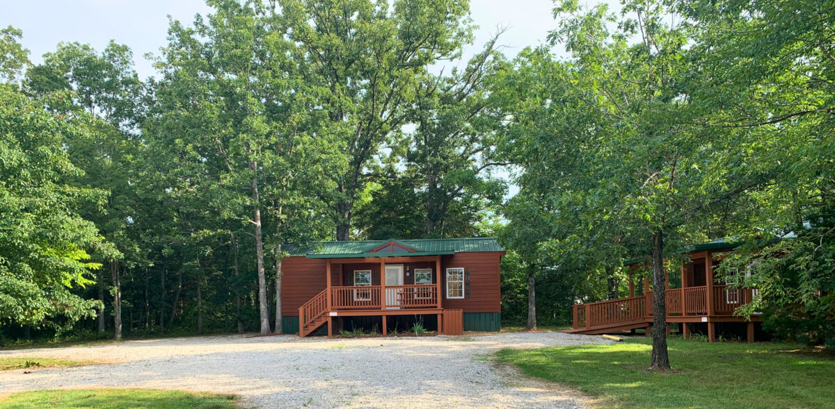 The exterior of cabins in a wooded area with a pond.
