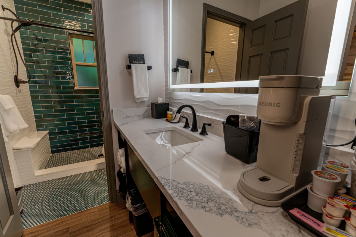 Renovated bathroom with a stone-look vanity, lighted mirror and tiled shower at Shamrock Court Motel