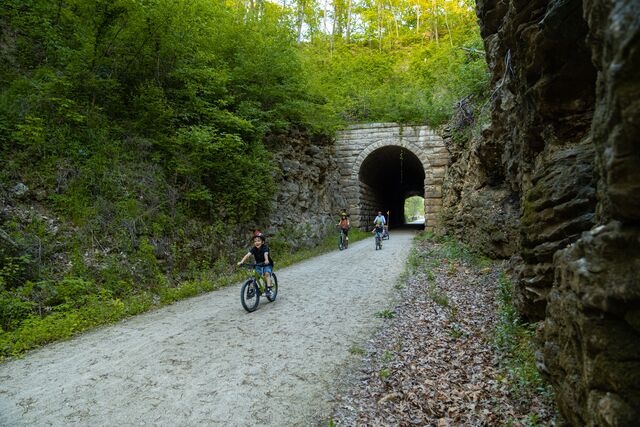 A family rides bicycles through a historic stone-and-brick tunnel on the Katy Trail rail-trail.
