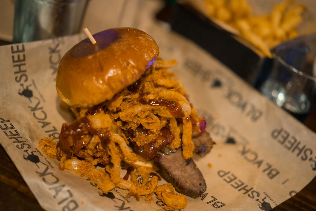A hamburger is topped with sliced brisket and friend onions.