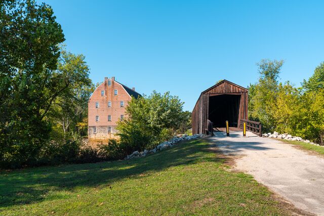 A three-story brick mill sits adjacent to a wooden covered bridge.