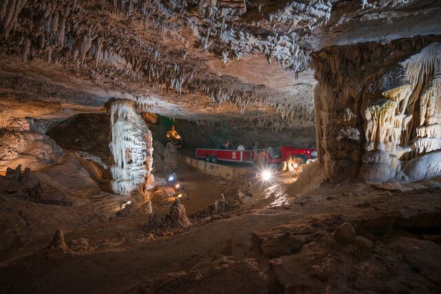 People aboard a red tram wind aroundock formations in a cave.