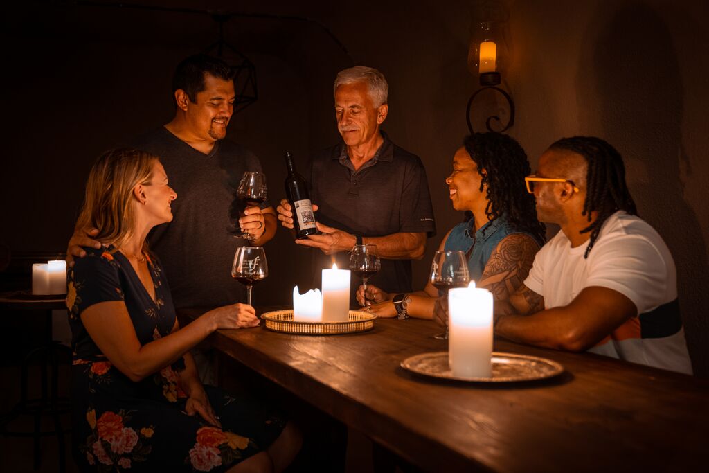 A group of five people sample wine by candlelight in the wine caves at Fence Style Vineyards, Winery and Distillery.